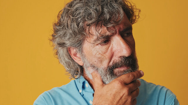 Close up portrait, elderly white-haired bearded man wears a blue shirt, shrugs her shoulders having no idea what to do next, isolated on an orange background in the studio