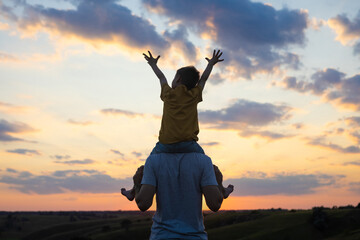 The boy sits on the shoulders of his father at sunset time. Father and son having fun together. Family, trust, protecting, care, parenting concept