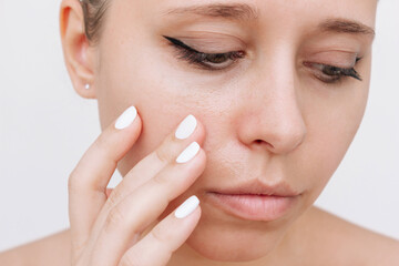 Young caucasian woman touching the face with her hand worried about the greasy skin isolated on a white background. Cosmetology and beauty concept. Oily skin, shine on the face