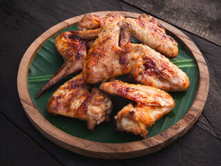 Grilled chicken wings in plate on wooden table background. Famous local Thai street food