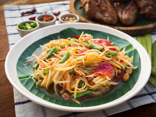 Papaya salad with grilled chicken wings on wooden background. Famous local Thai street food