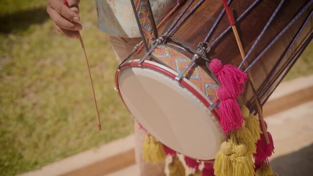 An Indian man playing dhol or drum during a baraat ceremony in an Indian wedding.