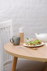 Breakfast on wooden table:zucchini waffles with cottage cheese, avakado and arugula in a white plate, cup of tea. Top view.