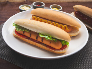 Hot dog with lettuce, tomatoes and mustard in plate on wooden table background. Fast food