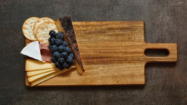 Charcuterie board time lapse. Top down view arrangement of meat, cheese and cracker appetizers on a wooden platter.