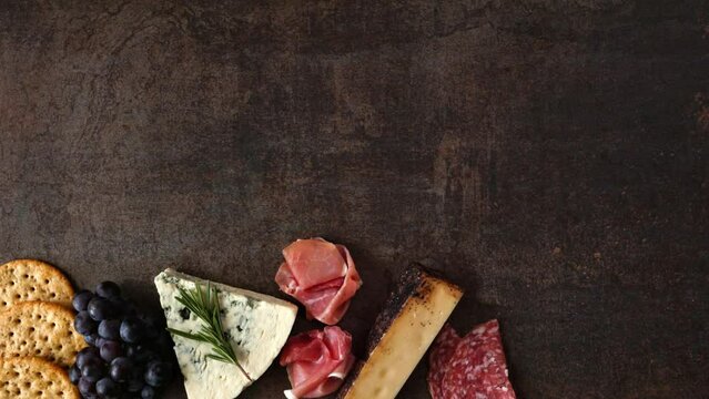 Charcuterie time lapse. Bottom border over a dark background with copy space. Above view arrangement of meat, cheese and cracker appetizers.