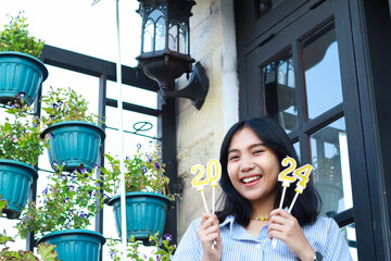 excited asian young woman smiling with holding 2024 number candle standing in outdoor terrace...