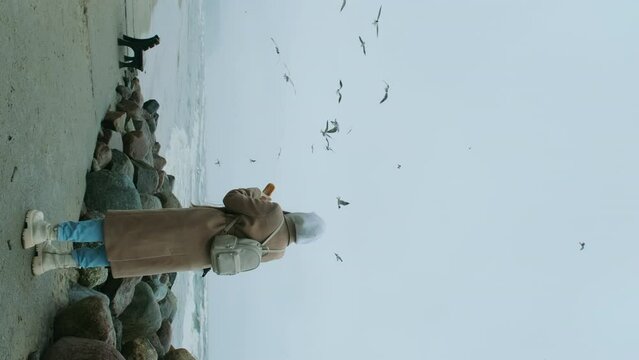 The girl is happy feeding seagulls with bread on the seashore.