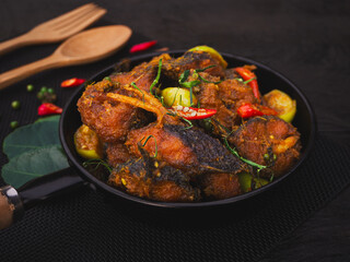 Stir fried catfish with herb and spicy sauce in pan on wooden background. Traditional Thai southern food