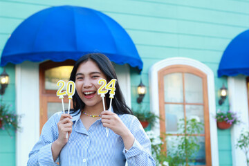 laughing asian young woman looking to camera enjoy 2024 new year eve celebration with holding 2024 number candle and standing in outdoor yard of vintage house - obrazy, fototapety, plakaty