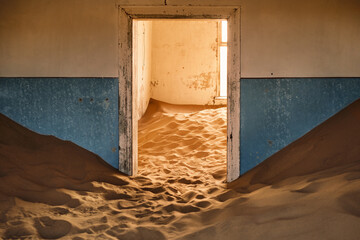 Interior of an abandoned building in Kolmanskop, Namibia, engulfed by sand and lit up by the warm light of the Namib Desert. Founded in 1908 for diamond exploration, the town was abandoned in 1956.