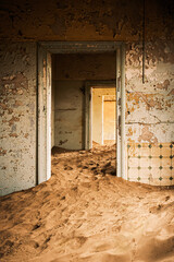 Interior of an abandoned building in Kolmanskop, Namibia, engulfed by sand and lit up by the warm light of the Namib Desert. Founded in 1908 for diamond exploration, the town was abandoned in 1956.