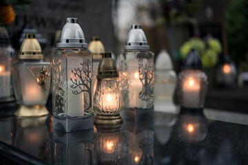 Lit grave candles with botanical motifs on a tombstone — Poland, November 1, All Saints’ Day...