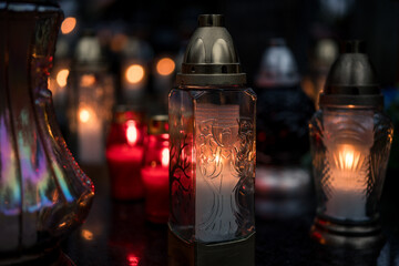 Decorative colored-glass grave candles glowing with warm candlelight on a tombstone at dusk —...