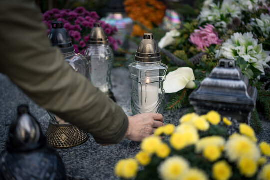 Hand placing a lit grave candle among flowers on a tombstone, close-up, Poland, November 1 &mdash; All Saints' Day (also known as All Souls' Day / Day of the Dead)