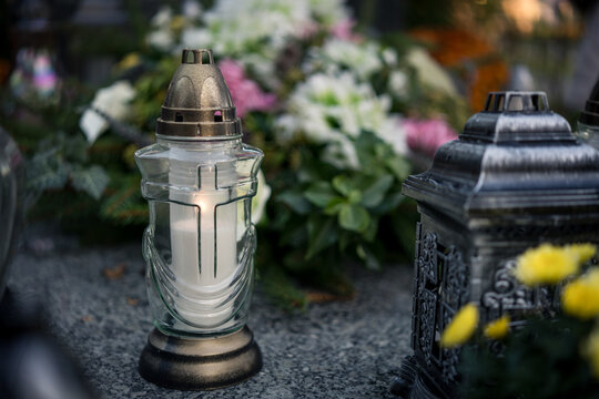 Lit grave candles among flowers on a grave at dusk &mdash; Poland, November 1, All Saints&rsquo; Day (also known as All Souls&rsquo; Day / Day of the Dead) decorations on the graves at evening