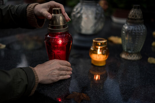 Hand placing a lit grave candle among flowers on a tombstone, close-up, Poland, November 1 &mdash; All Saints' Day (also known as All Souls' Day / Day of the Dead)