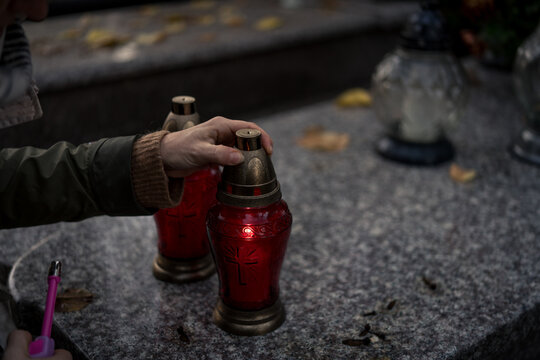 Hand placing a lit grave candle among flowers on a tombstone, close-up, Poland, November 1 &mdash; All Saints' Day (also known as All Souls' Day / Day of the Dead)