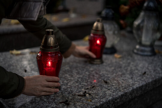 Hand placing a lit grave candle among flowers on a tombstone, close-up, Poland, November 1 &mdash; All Saints' Day (also known as All Souls' Day / Day of the Dead)
