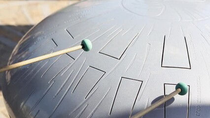 Playing a glucophone on a metal tongue drum with the help of special sticks. Melody audio tool for meditation, relaxation with deep magical sound
