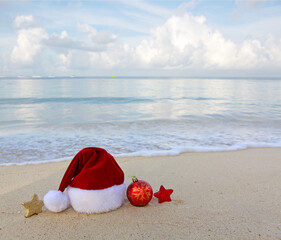 Merry Christmas background with red hat and decorations on Caribbean sand.