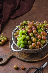 Green grapes in a metal colander on a brown concrete background with space for text.
