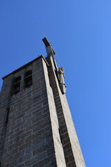 Bottom and side view of the stone tower of the Santuario da Penha in Guimaraes, Portugal. At the top it has a cross and a figure of Jesus Christ carved in stone. Vertical image.