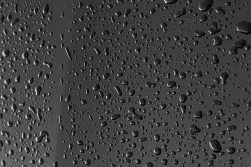 Rain or water drops different size on a black shiny car hood surface. Water droplets on dark iron surface and texture. Abstract background and water texture for design.