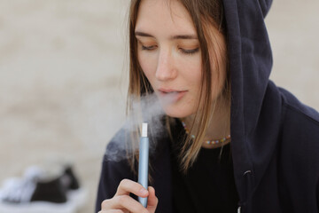Electronic cigarette technology. Young woman smokes and releases steam from hybrid cigarette device...