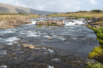 River with many picturesque cascades on Route 47 near Reykjavik, Iceland under sunny autumn cloudscape.