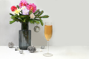Christmas creative bouquet of live fir branches in a vase, with chrysanthemum flowers, decorations and a glass of champagne on an elegant festive background. Christmas and New Year mockup for design 