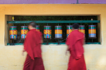 Buddhist monks passing and rotating prayer wheels on kora around Tsuglagkhang complex in McLeod...