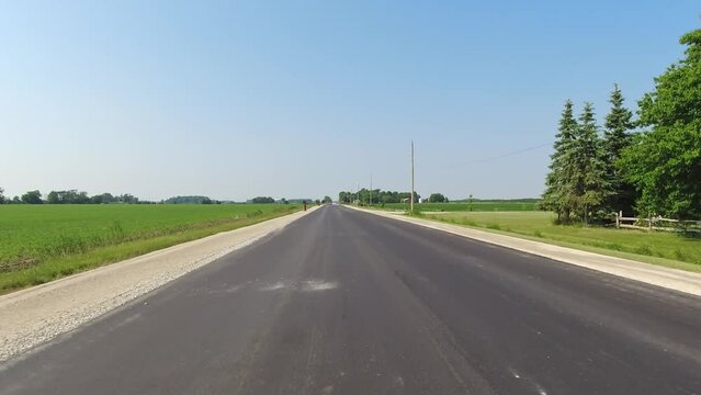 Back view Driving Plate looking backward. POV driving car view. Rural straight road. Summer daylight with farms lands  green fields and buildings. Road behind no traffic.