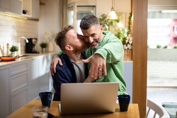 Young male gay couple announcing their engagement to a friend on a video call on the laptop in the living room at home