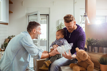 Young male gay couple unboxing stuff for the kitchen with their adopted child in their new apartment