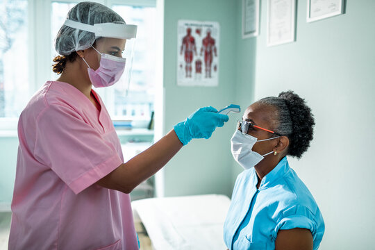 Young African American Female Health Worker Fever Screening Her Patient At The Clinic