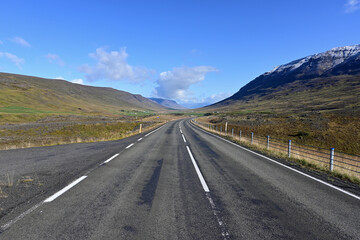 Ring Road near Akureyri, Iceland receding into distant curve between volcanoes under sunny morning autumn sky.
