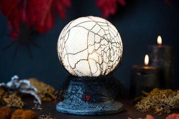 Glowing divination ball, candles and skeleton hand coming out of moss on fall background with spider. Halloween Scene.