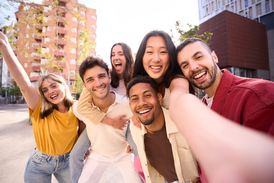 Big group of friends in piggyback taking selfie smiling at camera. Young people celebrating outside and having fun. Portrait of millennial guys and girls enjoying vacation. Multiracial best friends