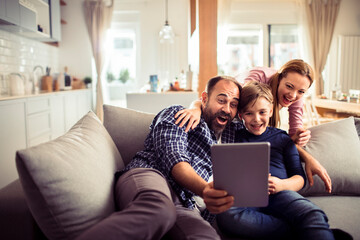 Young Caucasian family using a tablet and having fun on the couch at home