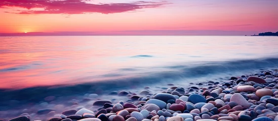 Schilderijen op glas Dreamy sunset photos with smooth water colorful sky and beach stones resembling wallpaper with a slight blur With copyspace for text © 2rogan
