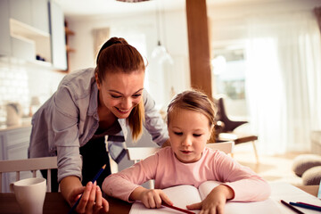 Loving young mother doing homework with her daughter at home