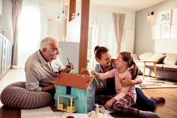 Multigenerational family painting a toy house together in the living room at home