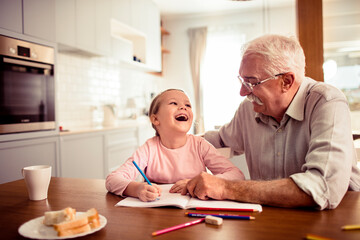 Young girl doing homework with the help of her grandfather at home