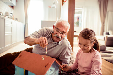 Young girl painting and being messy with her grandfather at home