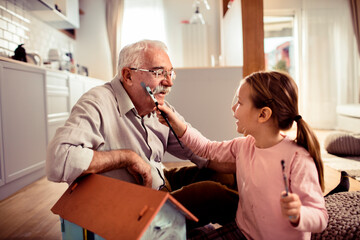 Young girl painting and being messy with her grandfather at home