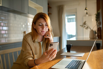 Young woman using her smartphone in the kitchen at home