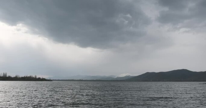 A panoramic view of Mountain Lake Sevan under a cloudy sky. The vastness of the lake is evident as low clouds touch the water, creating a dreamy reflection. Surrounding mountains add to the scene's