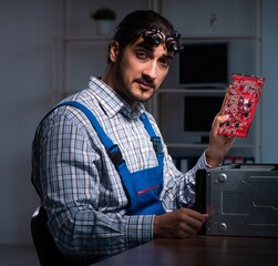 Young male technician repairing computer in workshop at night