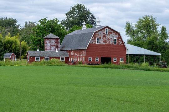 An Old Red Barn with Outbuildings viewed across a green field of grass.
